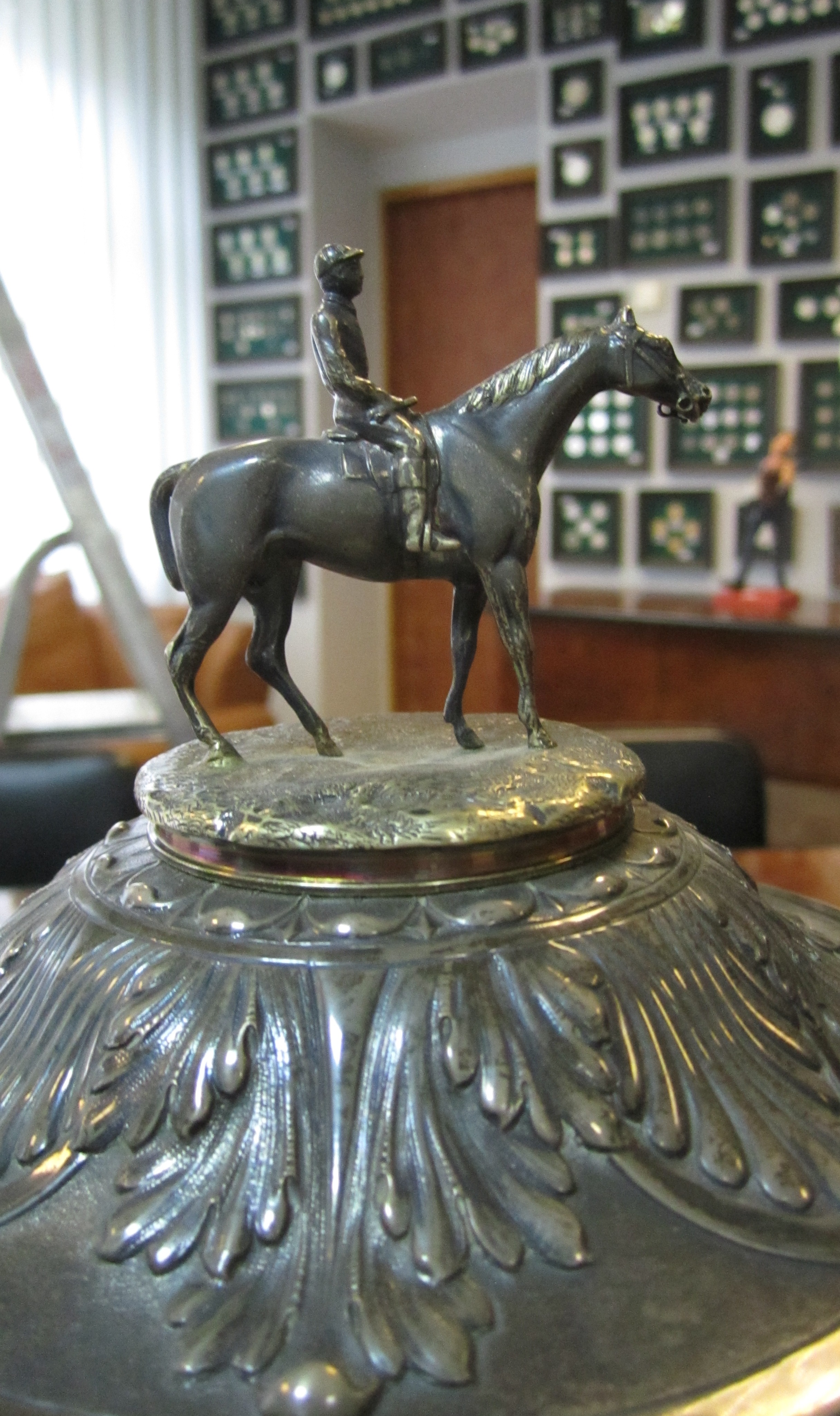 Чашка  виготовлена зі срібла 800 проби. Прикрашена позолоченою фігурою жокея на коні, чеканним зображенням скачок та орнаментом. Клейма на кришці f.M. , інв.№ 56242